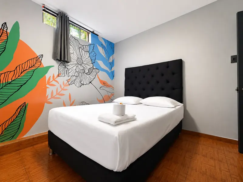 Mural de hojas verdes, azules y naranjas alrededor de la ventana, sobre pared gris