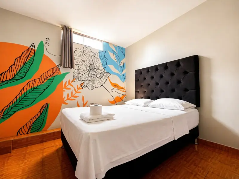 Habitación Matrimonial Superior con mural de sol naranja, hojas verdes y flor blanca sobre la cabecera