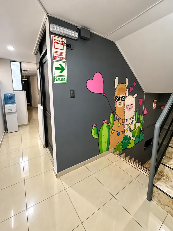 Pasillo del hostal con un mural pintado a mano de dos llamas junto a la escalera