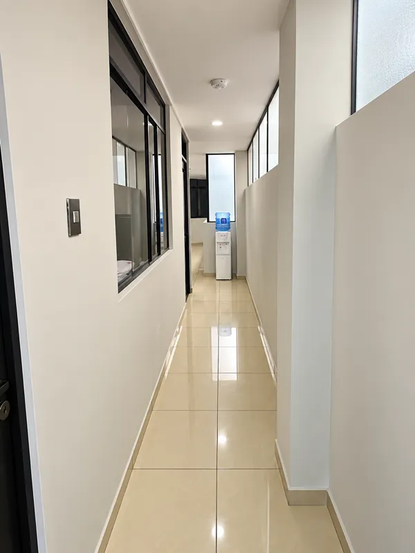 Pasillo del hostal con plantas junto a las ventanas y agua disponible para los huéspedes