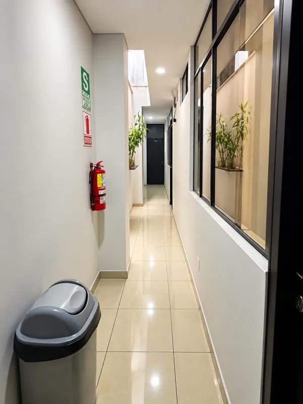Pasillo amplio e iluminado con ventanales interiores y plantas, acceso a las habitaciones privadas