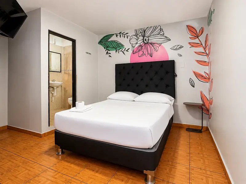 Habitación Queen con mural de flor sobre círculo rosa, mesa auxiliar y baño privado a la vista