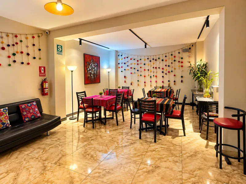 Sala común del Llama Llama Hostel con sofá de cuero, mesas con manteles andinos de colores y guirnaldas de pompones — el espacio de coworking y desayuno