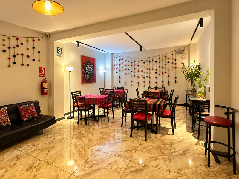 Rincón de estar de la sala con sofá de cuero y cojines bordados, abierto al espacio principal de mesas