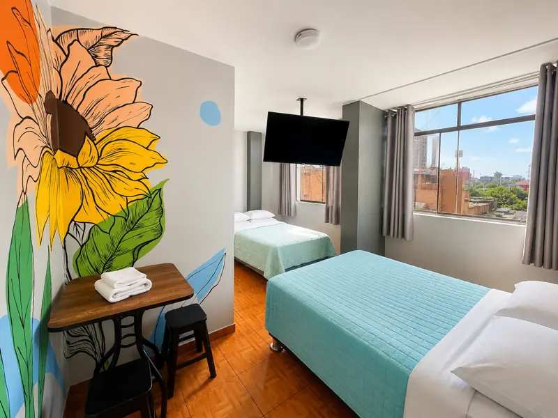 Habitación con dos camas, un gran girasol pintado en la pared y ventana con vista a Lima